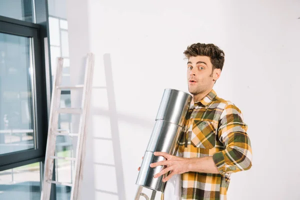 Handsome young man looking at camera while holding cans with paint — Stock Photo