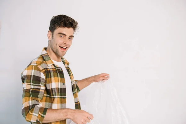 Smiling young man holding cellophane while preparing for wall painting — Stock Photo