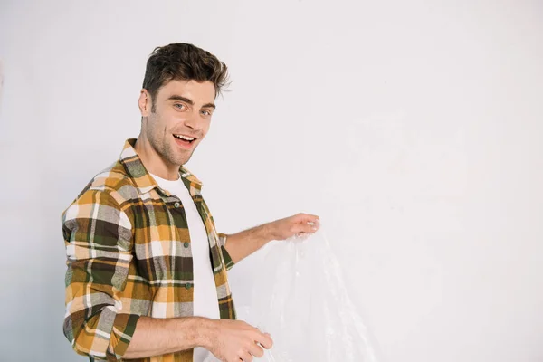 Joven sonriente sosteniendo celofán mientras se prepara para la pintura de la pared - foto de stock