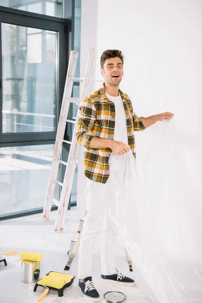 Handsome young man holding cellophane while preparing for wall painting — Stock Photo