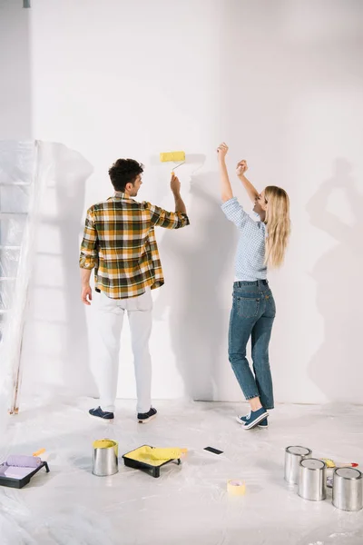Alegre joven mujer bailando mientras novio holding amarillo pintura rodillo - foto de stock