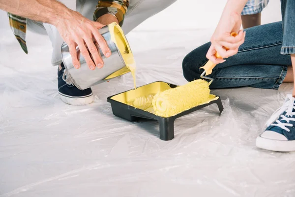 Cropped view of man adding yellow paint into roller tray and woman holding paint roller — Stock Photo