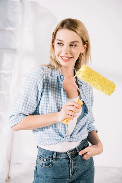 Attraktive junge Frau lächelt, während sie eine gelbe Farbwalze in der Hand hält — Stockfoto