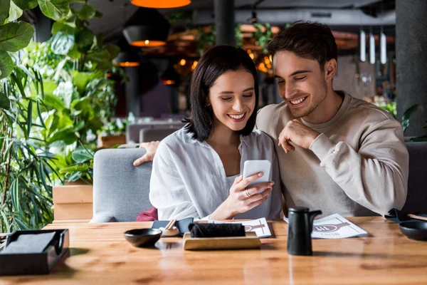 Happy man and woman looking at smartphone in sushi bar — Stock Photo