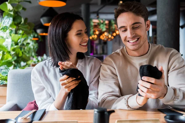 Hombre alegre y mujer feliz sosteniendo servilletas negras en sushi bar - foto de stock