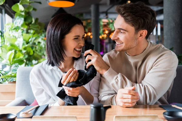 Felice uomo che tiene il tovagliolo nero vicino al volto della donna sorridente — Foto stock