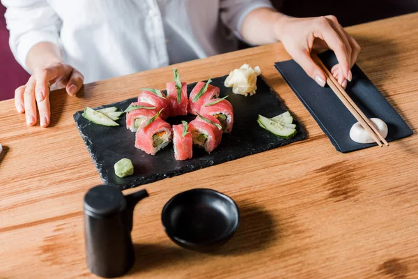 Vista cortada de mulher tocando pauzinhos perto de sushi saboroso — Fotografia de Stock
