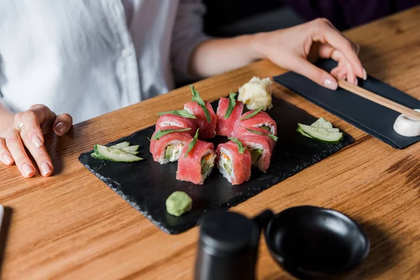 Vue recadrée de jeune femme touchant baguettes près de savoureux sushi — Photo de stock