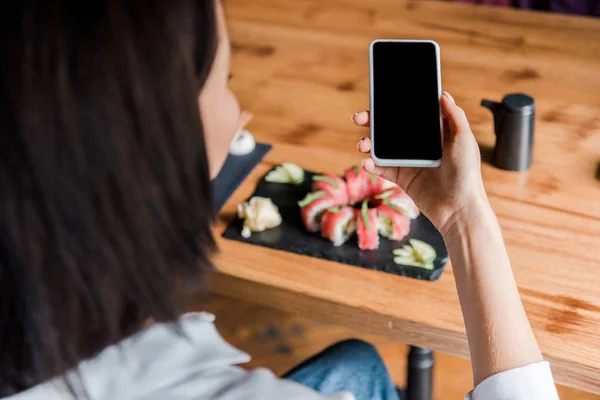 Selective focus of woman holding smartphone with blank screen near tasty sushi in restaurant — Stock Photo