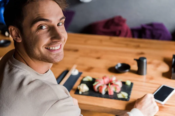 Foco seletivo do homem feliz perto do smartphone com tela em branco e sushi saboroso no restaurante — Fotografia de Stock