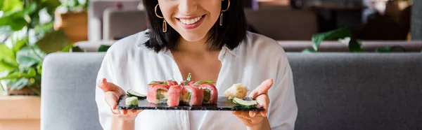 Панорамный снимок счастливой женщины, держащей тарелку с вкусными суши — стоковое фото