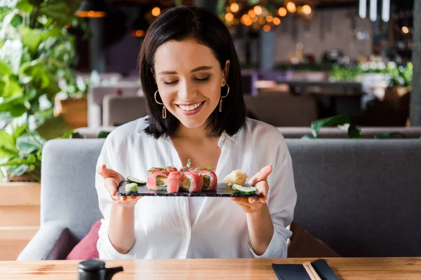 Donna felice che tiene il piatto con sushi saporito in ristorante — Foto stock