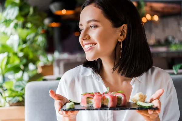 Mulher alegre segurando prato com sushi saboroso no restaurante — Fotografia de Stock