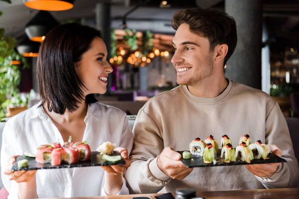 Uomo felice e donna allegra sorridente mentre tiene piatti con sushi — Foto stock