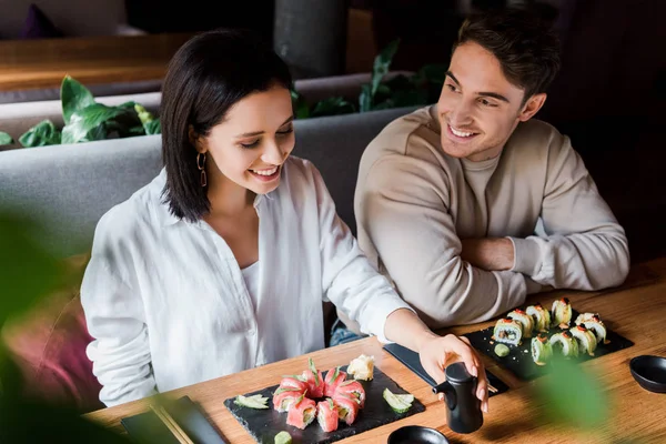 Foco seletivo do homem feliz olhando para a mulher alegre sorrindo perto de placas com sushi — Fotografia de Stock