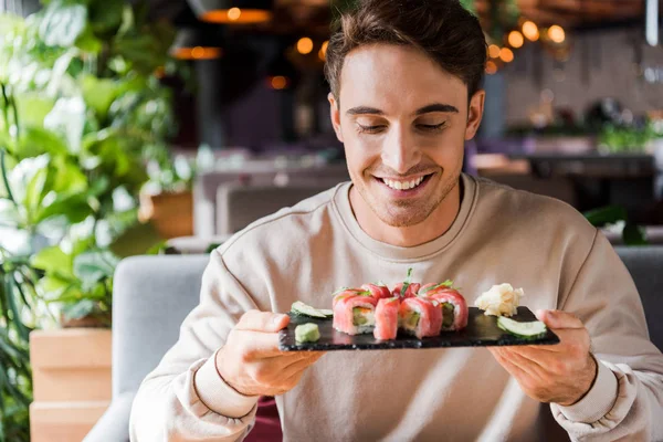 Uomo felice guardando piatto con sushi saporito in ristorante — Foto stock