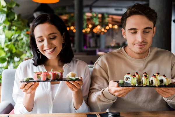 Homem feliz e mulher alegre sorrindo enquanto segurando placas com sushi saboroso — Fotografia de Stock