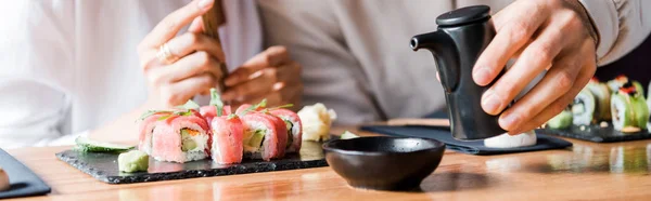 Panoramic shot of man holding black bottle near woman and sushi — Stock Photo