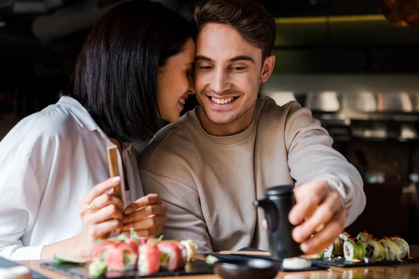 Fuoco selettivo dell'uomo allegro che tiene la bottiglia nera vicino alla donna e al sushi — Foto stock