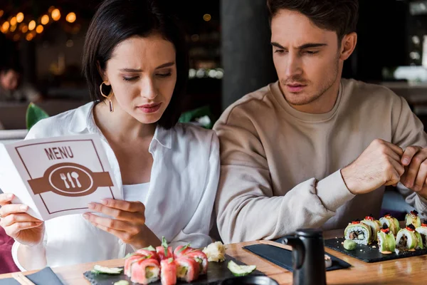 Hombre guapo sentado cerca de mujer atractiva con menú en las manos - foto de stock