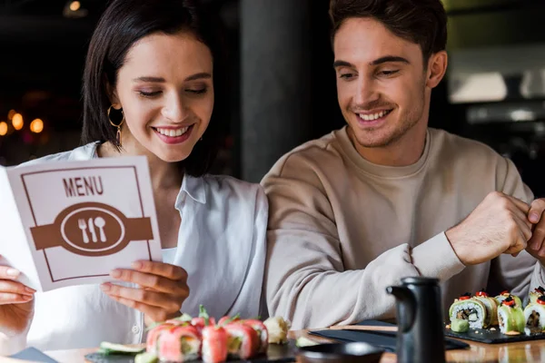 Красивый мужчина сидит рядом с счастливой женщиной с меню в руках — стоковое фото