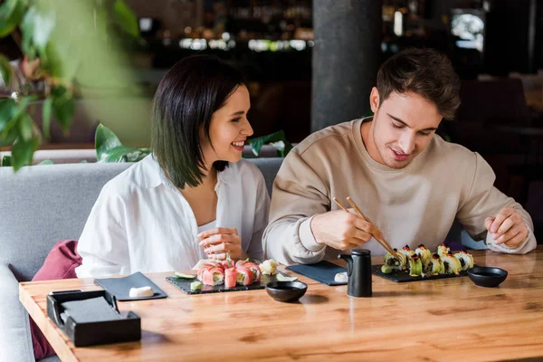 Enfoque selectivo de hombre y mujer feliz cerca de sushi sabroso en el restaurante - foto de stock