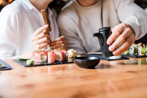 Cropped view of man holding black bottle near woman in sushi bar — Stock Photo