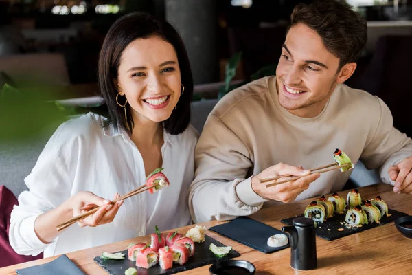 Щасливий чоловік і жінка тримають палички зі смачними суші в ресторані — стокове фото