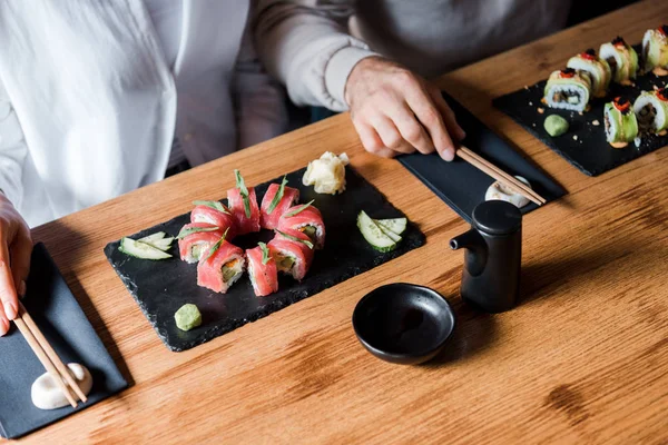 Cropped view of man and woman touching chopsticks near tasty sushi in restaurant — Stock Photo