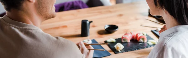 Panoramic shot of man holding chopsticks near young woman in sushi bar — Stock Photo