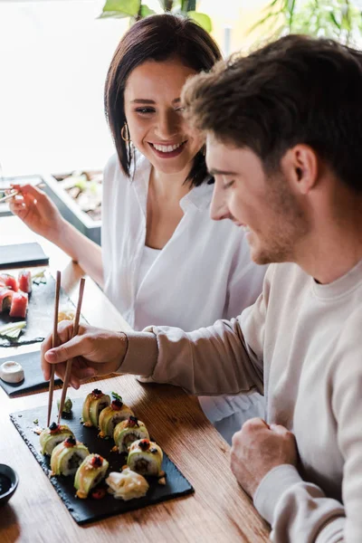 Enfoque selectivo de la mujer joven mirando al hombre en el bar de sushi - foto de stock