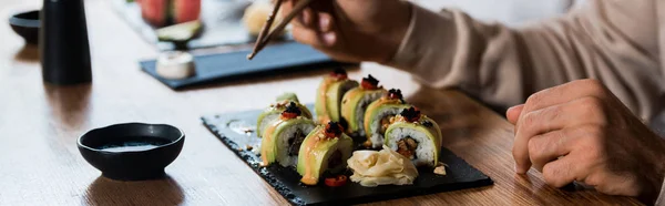 Panoramaaufnahme eines Mannes, der Essstäbchen in der Nähe von Tellern mit Sushi hält — Stockfoto