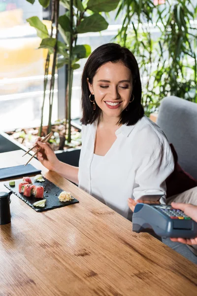 Ausgeschnittene Ansicht von Kellner mit Kreditkartenlesegerät in der Nähe von Frau, die mit Smartphone bezahlt — Stockfoto