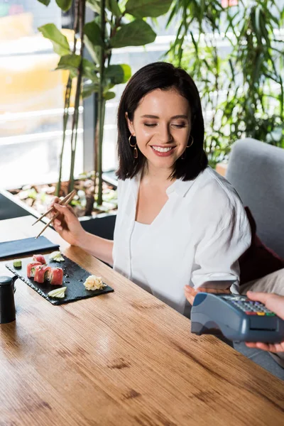 Vue recadrée du serveur tenant lecteur de carte de crédit près de la femme payant avec smartphone — Photo de stock