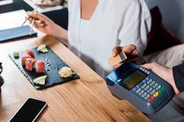 Обрезанный вид официанта, держащего читателя кредитных карт рядом с женщиной, платящей кредитной картой — стоковое фото