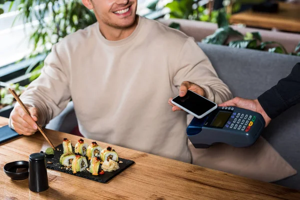 Ausgeschnittene Ansicht eines Mannes mit Smartphone und leerem Bildschirm in der Nähe von Kreditkartenlesegerät — Stockfoto