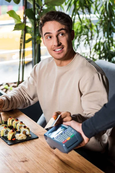 Selective focus of handsome man holding credit card near credit card reader — Stock Photo