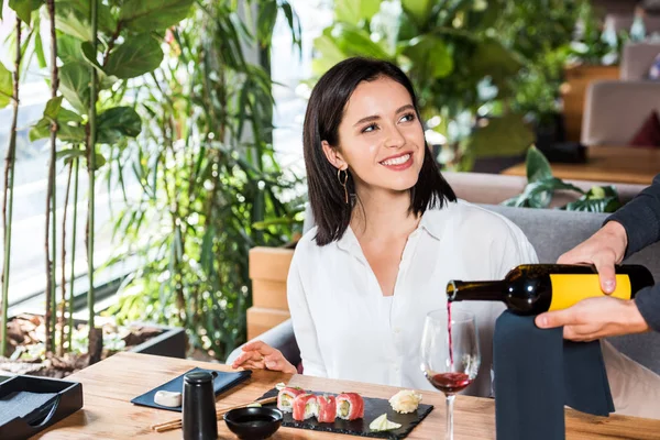 Vista ritagliata del cameriere versando vino rosso in vetro vicino donna attraente — Foto stock