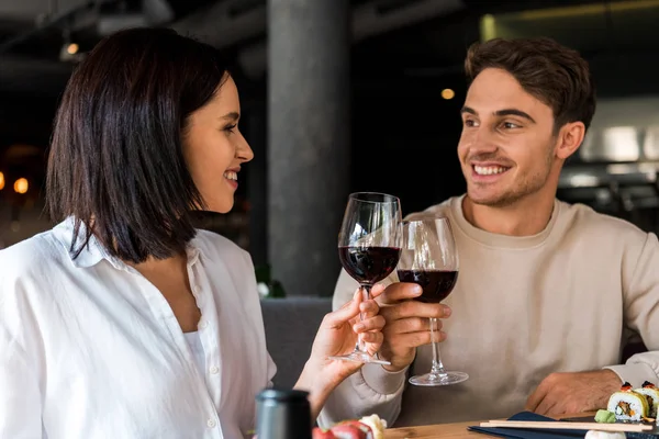 Homem feliz e mulher alegre clinking copos com vinho tinto perto de sushi — Fotografia de Stock