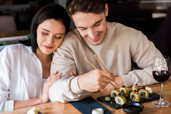 Happy man holding chopsticks near sushi near attractive woman — Stock Photo