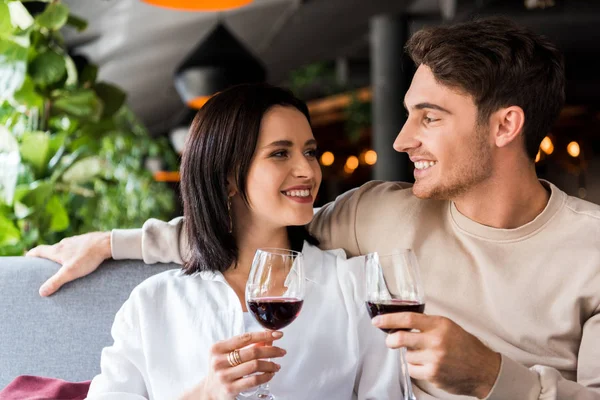 Hombre feliz y mujer alegre sosteniendo vasos con vino tinto - foto de stock