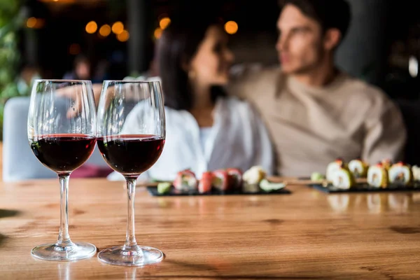 Selektiver Fokus von Gläsern mit Rotwein in der Nähe glücklicher Männer und Frauen — Stockfoto