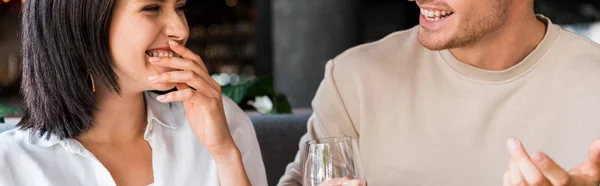 Tiro panorámico de hombre feliz gesto cerca de la mujer riendo en el restaurante - foto de stock