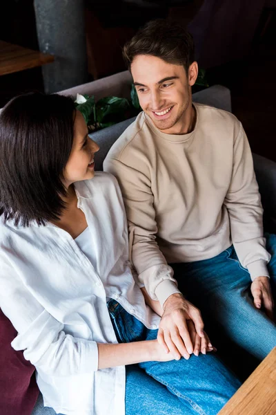 Hombre y mujer felices tomados de la mano mientras están sentados en el restaurante - foto de stock