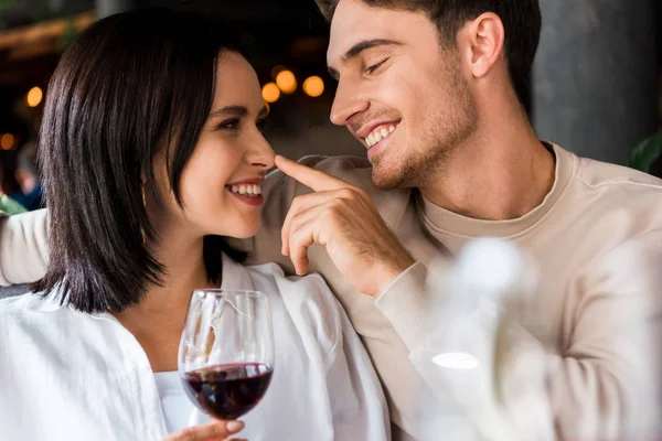 Happy man touching nose of girlfriend with red wine in glass — Stock Photo