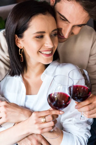 Hombre feliz sosteniendo copa con vino cerca de chica alegre - foto de stock