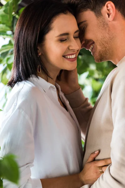 Selective focus of handsome man with closed eyes hugging cheerful girlfriend in restaurant — Stock Photo