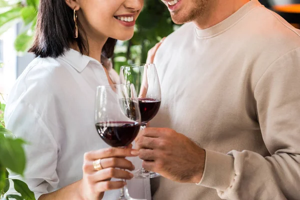 Vista cortada de homem feliz segurando vidro com vinho tinto perto menina alegre — Fotografia de Stock