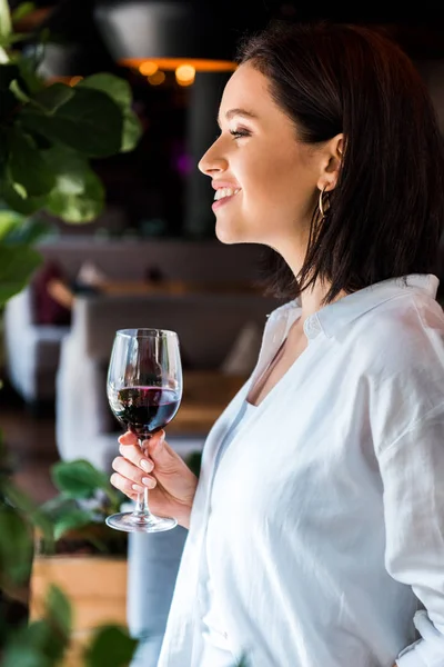 Vue latérale de femme gaie tenant un verre avec du vin rouge — Photo de stock