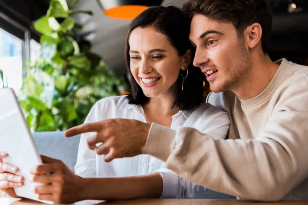 Счастливый мужчина показывает пальцем на ноутбук рядом с женщиной в ресторане — стоковое фото